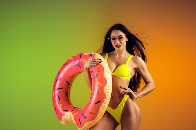 Moda portret młodej wysportowanej i wysportowanej kobiety z gumowym pączkiem w stylowych żółtych strojach kąpielowych na gradientowej ścianie idealne ciało gotowe na lato