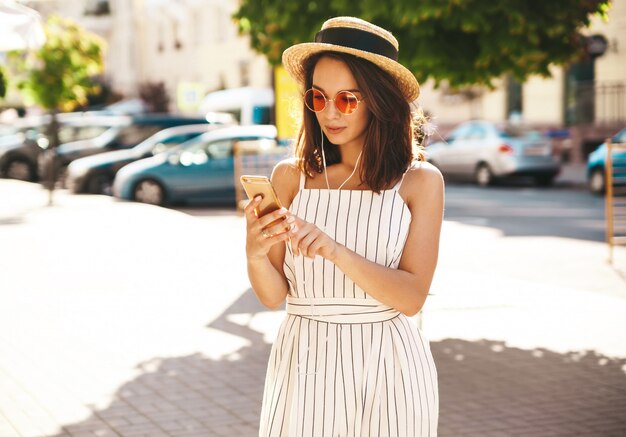 model brunetka w letnie ubrania pozowanie na ulicy przy użyciu telefonu komórkowego