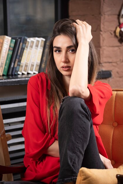 Model młoda kobieta w czerwonej bluzce siedzi i pozuje.