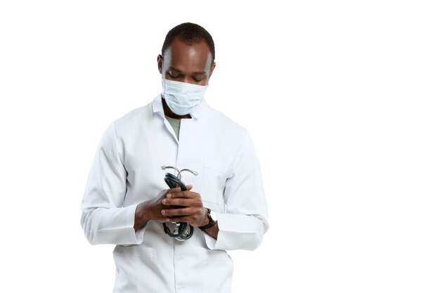Modlitwa za Boga. Mężczyzna młody lekarz ze stetoskopem i maską na twarz na białym studio.
