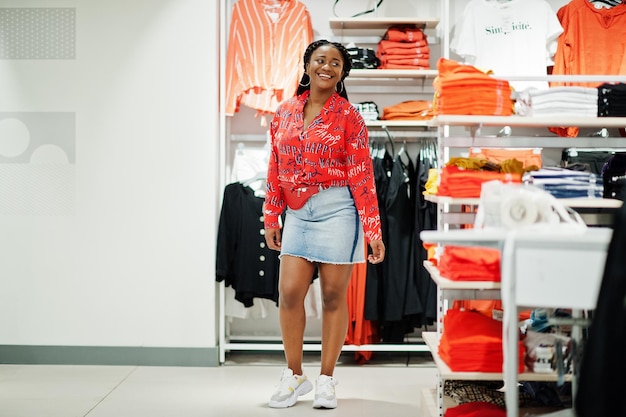 Modna afroamerykanka w spódnicy jeansowej czerwonej koszuli z torbą crossbody postawiona w sklepie z ubraniami Czas na zakupy
