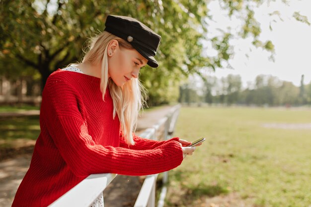 Modna blondynka w modne ubrania trzymając telefon. Urocza kobieta younf stojąca z inspiracją.