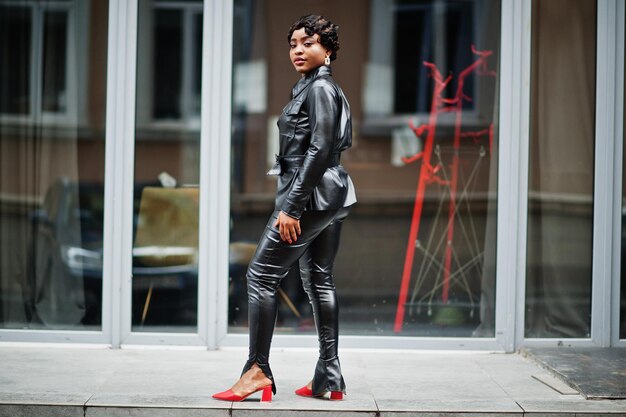 Modna piękna afroamerykanka pozuje w czarnej skórzanej kurtce i spodniach na ulicy