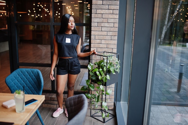 Modne feministyczne afroamerykanki noszą czarną koszulkę i szorty pozowane w restauracji