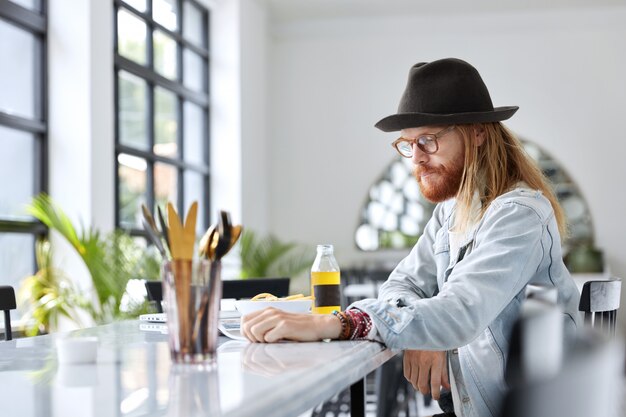 Modny hipster facet ubrany w stylowy czarny kapelusz i dżinsową koszulę