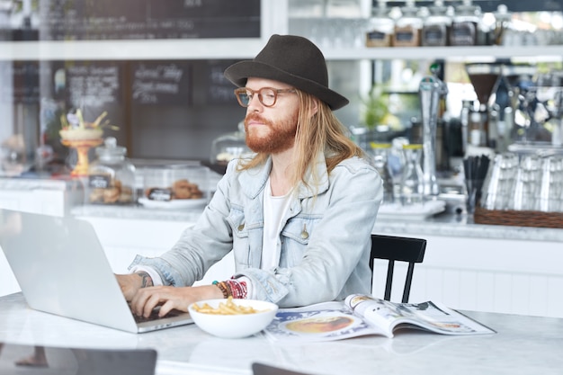 Modny hipster facet ubrany w stylowy czarny kapelusz i dżinsową koszulę