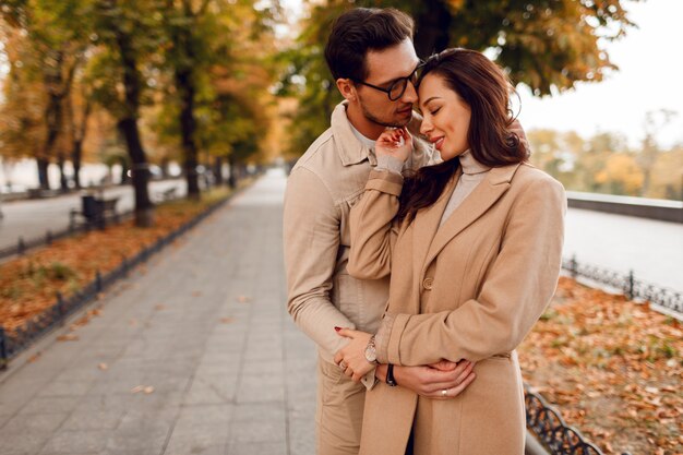Modny mężczyzna i kobieta zawstydzający podczas randkowania w jesiennym parku. Nosi stylowe beżowe płaszcze. Romantyczny nastrój.