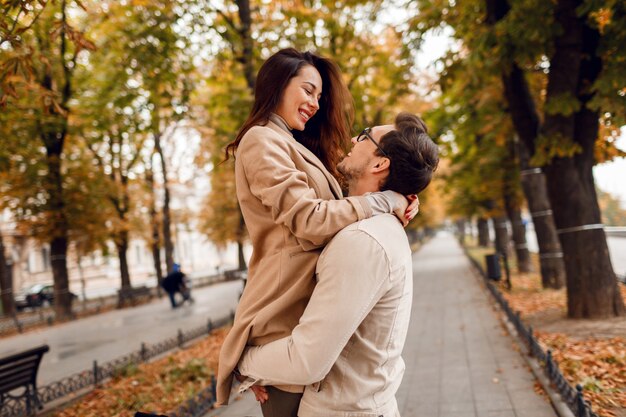 Modny mężczyzna i kobieta zawstydzający podczas randkowania w jesiennym parku. Nosi stylowe beżowe płaszcze. Romantyczny nastrój.