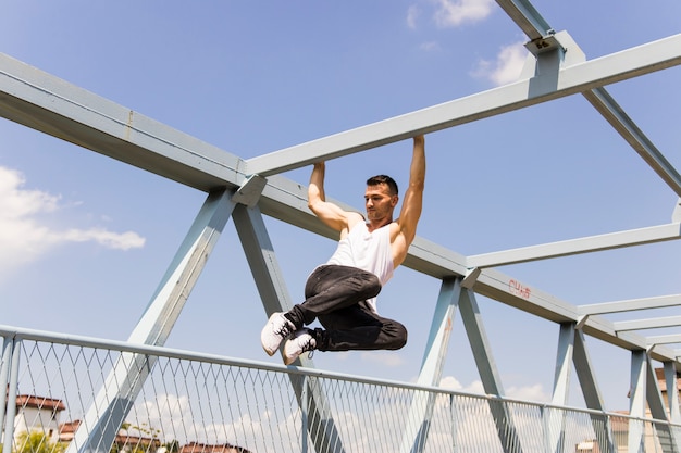 Bezpłatne zdjęcie modny młody człowiek wisi na pręcie mostu