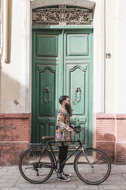 Modny młody człowiek z jego rowerową pozycją przed zielonym drzwi