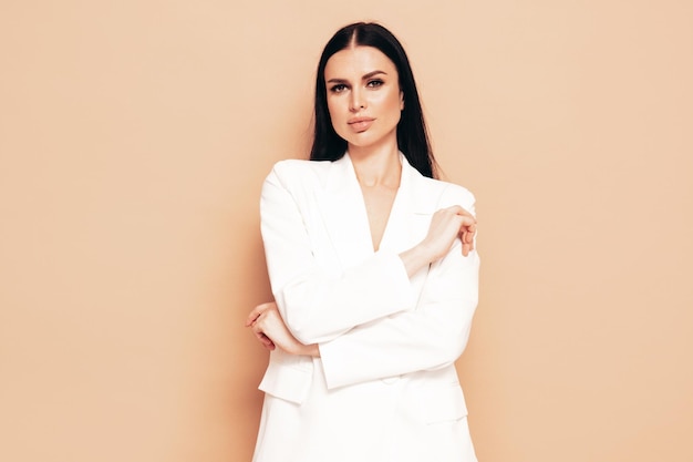 Mody portret młodej pięknej kobiety brunetka ubrana w ładny modny biały garnitur Seksowna modelka pozowanie w studio Modna kobieta na beżowym tle