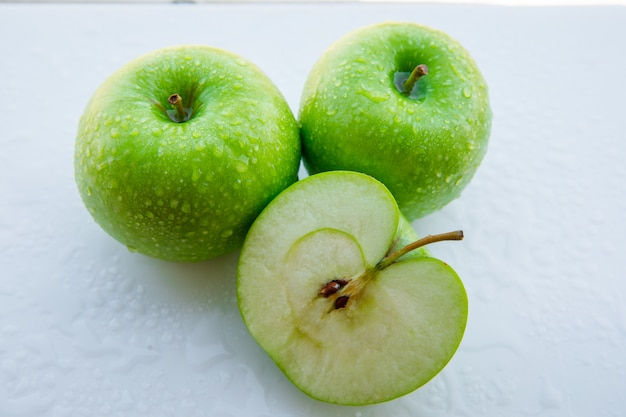Mokre zielone jabłka i połowa na białym. zbliżenie.