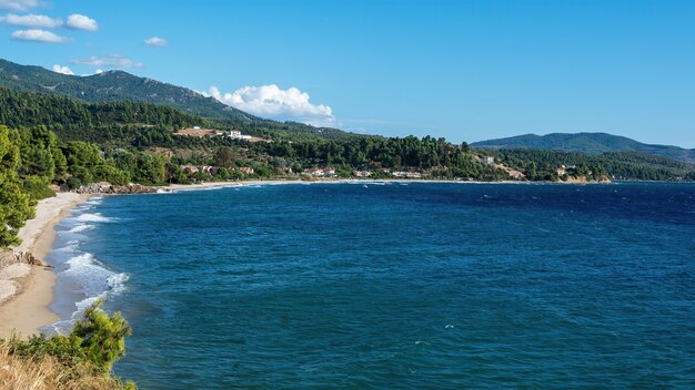 Morze Egejskie wybrzeże Grecji, skaliste wzgórza porośnięte drzewami i krzewami, zabudowania położone blisko wybrzeża
