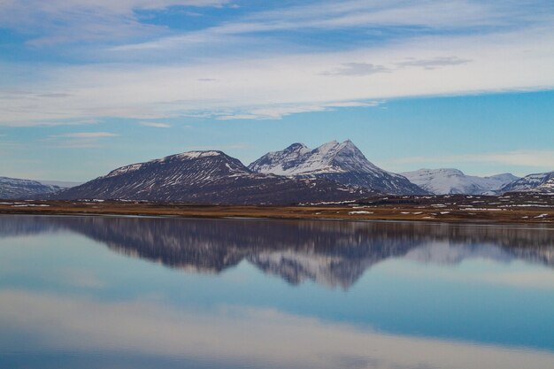Morze otoczone przez skaliste góry pokryte śniegiem i odbijające się w wodzie na Islandii