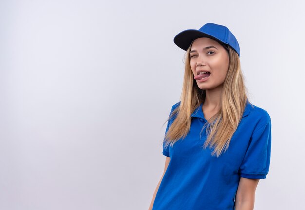 mrugająca młoda kobieta dostawy, ubrana w niebieski mundur i czapkę pokazującą język