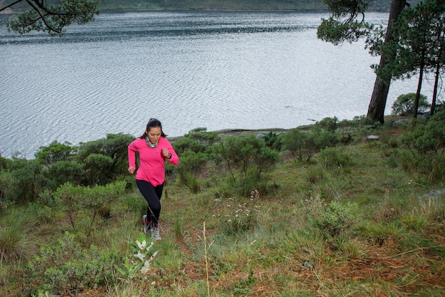 Mujer corriendo en el bosque subiendo montanas con un lago al fondo