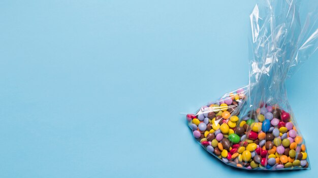 Multicoloured klejnotów cukierki w plastikowym worku na błękitnym tle