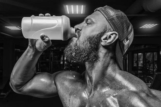 Muskularny mężczyzna na siłowni pije z shakera. koncepcja fitness i kulturystyka.