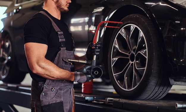 Muskularny mężczyzna naprawia koło samochodu specjalnym narzędziem w serwisie samochodowym.