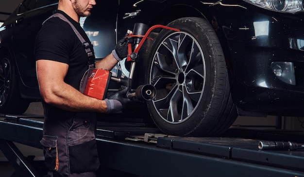 Muskularny mężczyzna naprawia koło samochodu specjalnym narzędziem w serwisie samochodowym.