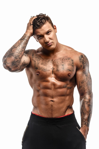 Bezpłatne zdjęcie muskularny mężczyzna półnagi macho z tatuażami pozuje w studio na białym tle