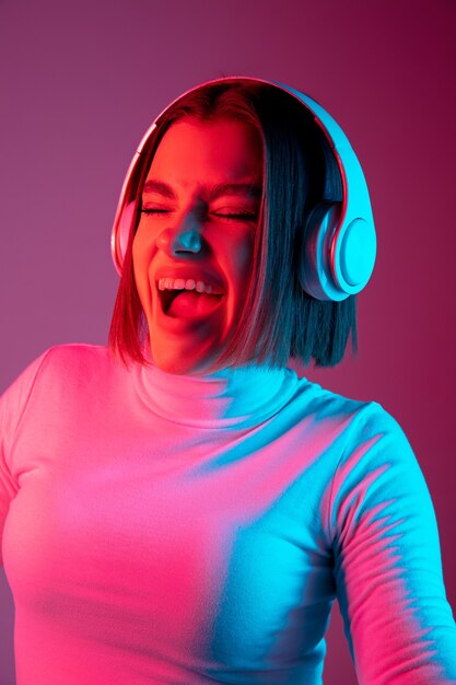 Muzyka. Portret kobiety kaukaski na różowym tle studio w modnym świetle neonu. Piękna modelka ze słuchawkami. Pojęcie ludzkich emocji, wyraz twarzy, sprzedaż, reklama, moda.