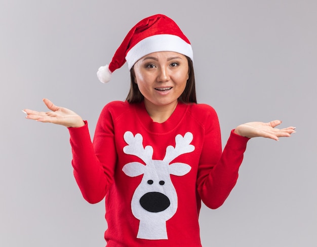 Mylić młoda azjatycka dziewczyna ubrana w świąteczny kapelusz z swetrem, rozkładając ręce na białym tle