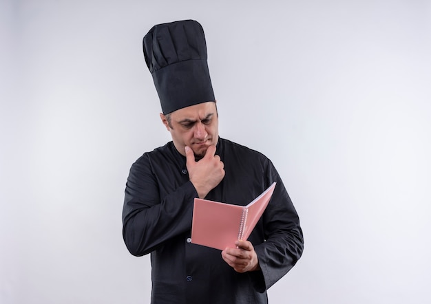 Myślenie kucharza w średnim wieku mężczyzna w mundurze szefa kuchni patrząc na notatnik w ręku