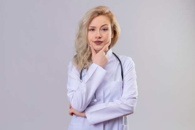 Myślenie lekarza młoda dziewczyna ubrana w stetoskop w sukni medycznej położyła rękę na szczęce na białym tle