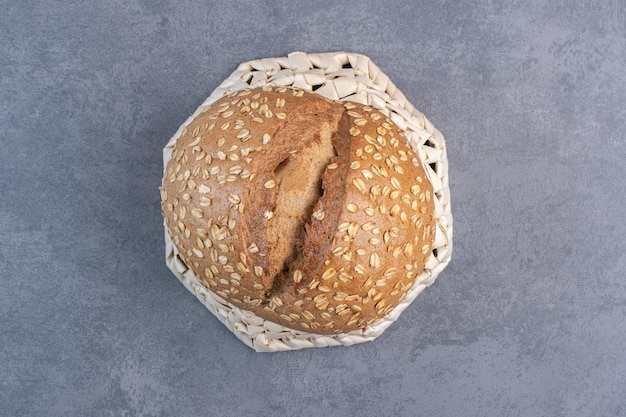 Nakładanie płatków na bochenek chleba na odwróconym koszu na marmurowym tle. Zdjęcie wysokiej jakości