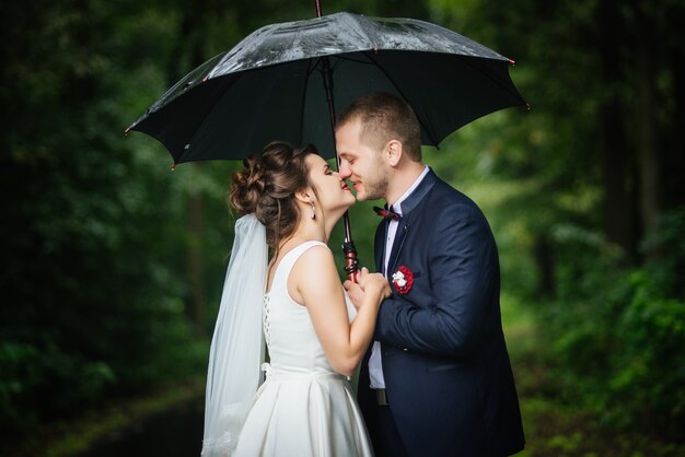 Narzeczeni trzymając parasol w ręce patrząc na siebie, całując i uśmiechając się