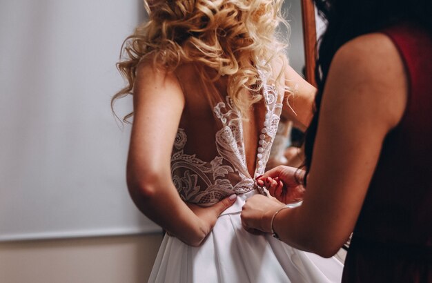 narzeczona blondynka ubiera piękną sukienkę kobieta pomaga jej przycisk z tyłu