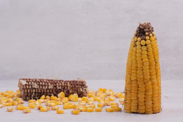 Nasiona kukurydzy i pół gotowanej kukurydzy na białym stole.