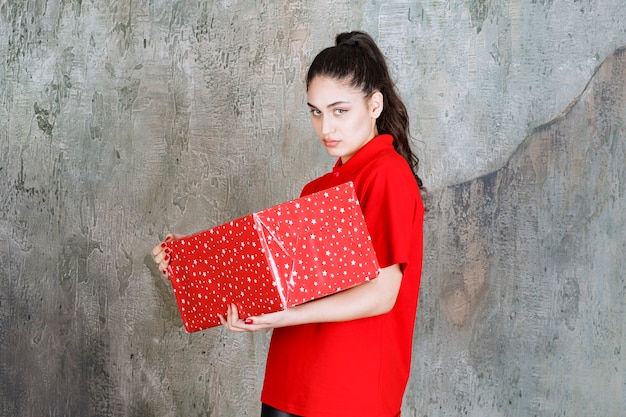 Bezpłatne zdjęcie nastolatek dziewczyna trzyma czerwone pudełko z białymi kropkami, wygląda na niezadowoloną i odmawia czegoś.