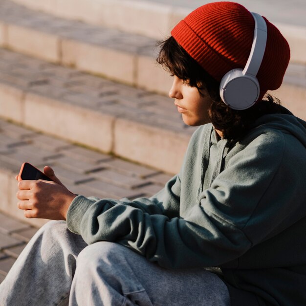 Nastolatek na zewnątrz przy użyciu smartfona i słuchanie muzyki na słuchawkach