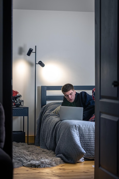 Nastolatek Siedzi W Pokoju Na łóżku I Korzysta Z Laptopa