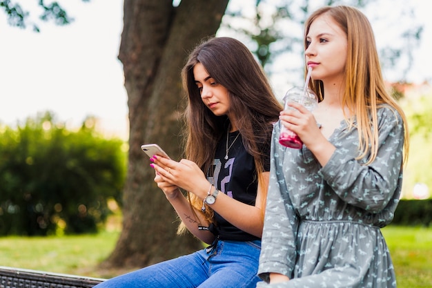 Bezpłatne zdjęcie nastolatki pije w pobliżu przyjaciela z smartphone