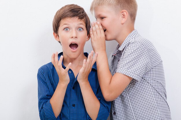 Nastoletni chłopak szepczący do ucha sekret dla przyjaciela