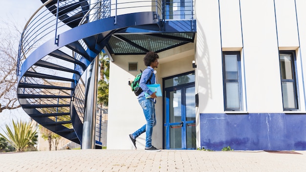 Nastoletni chłopiec trzyma książkę w ręku spaceru przed budynkiem uniwersytetu