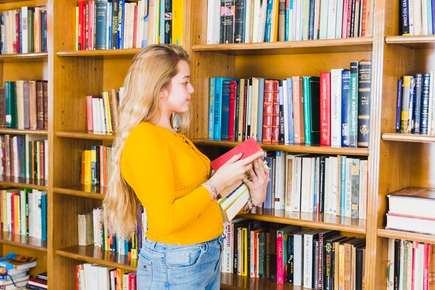 Nastoletnia dziewczyna bierze książki z bibliotecznej półki