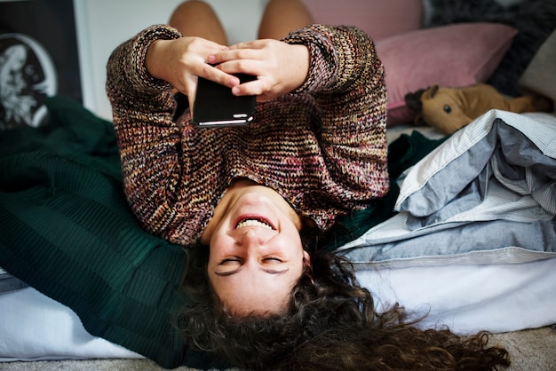 Nastoletnia dziewczyna używa smartphone na łóżkowym ogólnospołecznym środka i nałogu pojęciu