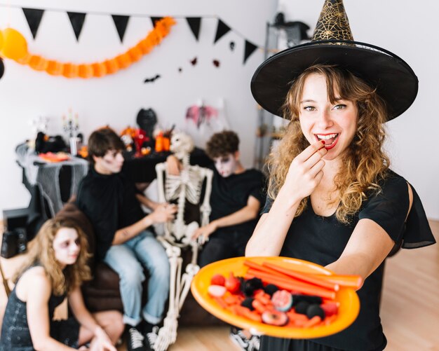 Nastoletnia dziewczyna w czarownica kostiumu seansu talerzu z marmoladowym i uśmiechniętym