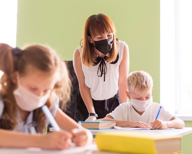 Nauczyciel i dzieci chroniące się maskami na twarz w klasie