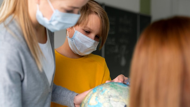 Bezpłatne zdjęcie nauczycielka z maską medyczną uczy geografii z kulą ziemską w klasie