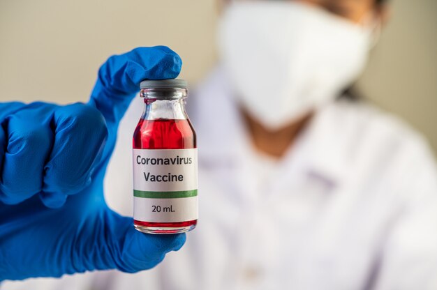 Naukowcy w maskach i rękawiczkach, niosący fiolki ze szczepionkami w celu ochrony Covid-19