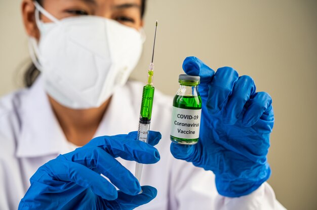 Naukowcy w maskach i rękawiczkach Trzymający strzykawkę ze szczepionką, aby zapobiec Covid-19