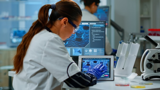 Naukowiec korzystający z cyfrowego tabletu pracujący w nowoczesnym laboratorium badań medycznych, analizujący informacje DNA. Medycyna, badania biotechnologiczne w zaawansowanym laboratorium farmaceutycznym, badanie ewolucji wirusa