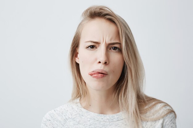 Negatywna ludzka reakcja, uczucia i postawa. Close-up portret zdegustowanej, skrzywionej blondynki kobiety w zwykłym ubraniu krzywiący się, wystający język, mdłości z powodu nieprzyjemnego zapachu lub smrodu