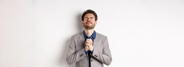 Bezpłatne zdjęcie nerwowy przedsiębiorca w garniturze błagający boga trzymającego się za ręce w modlitwie z błagalnym wyrazem blisko e