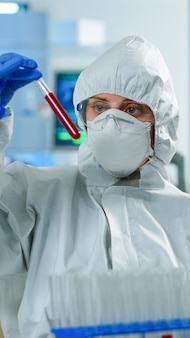 Neurolog w kombinezonie ppe pracujący przy opracowywaniu szczepionek, analizujący próbkę krwi w wyposażonym laboratorium, piszący na komputerze. zespół badający ewolucję wirusa przy użyciu zaawansowanych technologii w badaniach nad leczeniem covid1